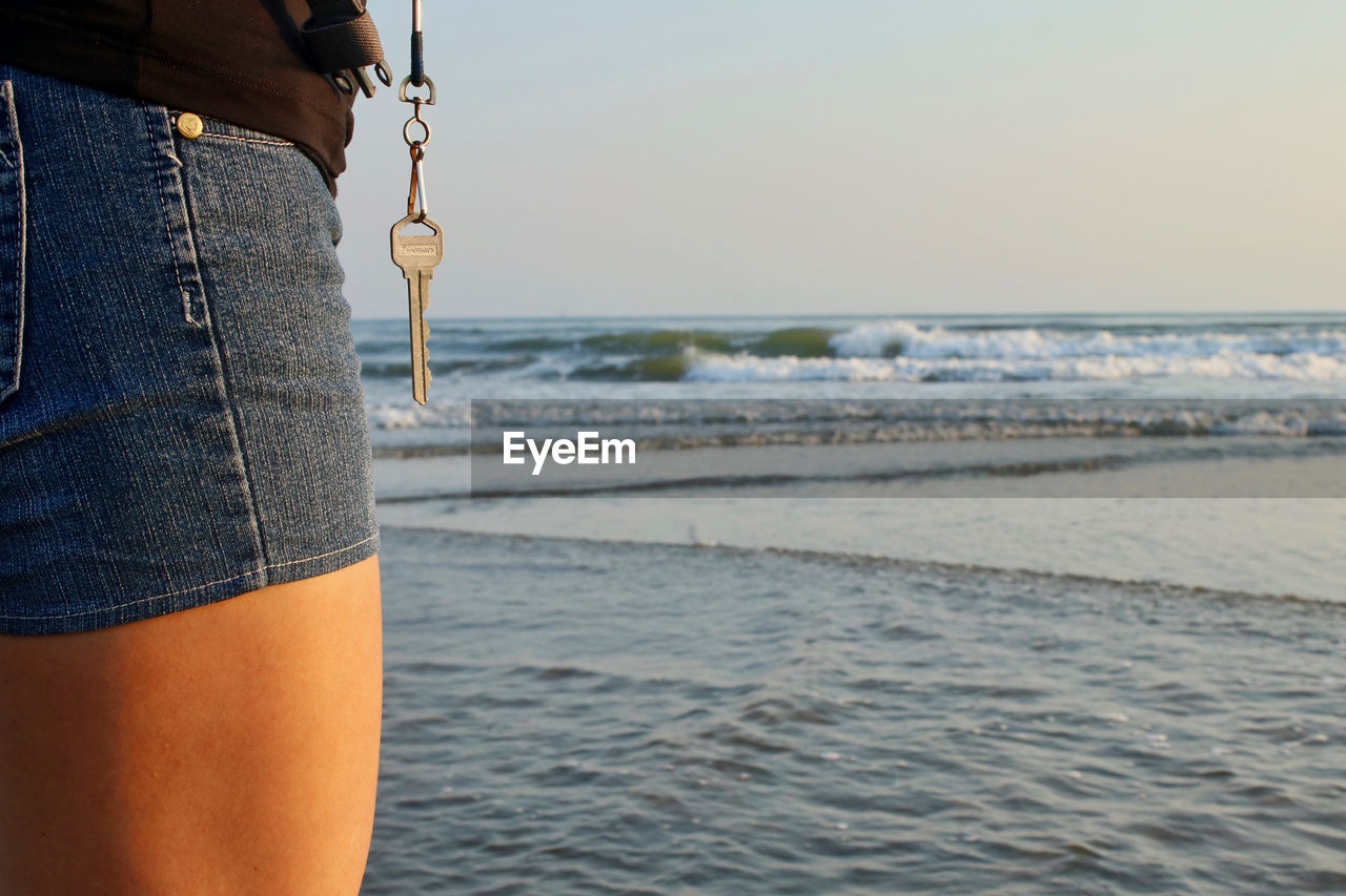 MIDSECTION OF MAN HOLDING UMBRELLA AT BEACH