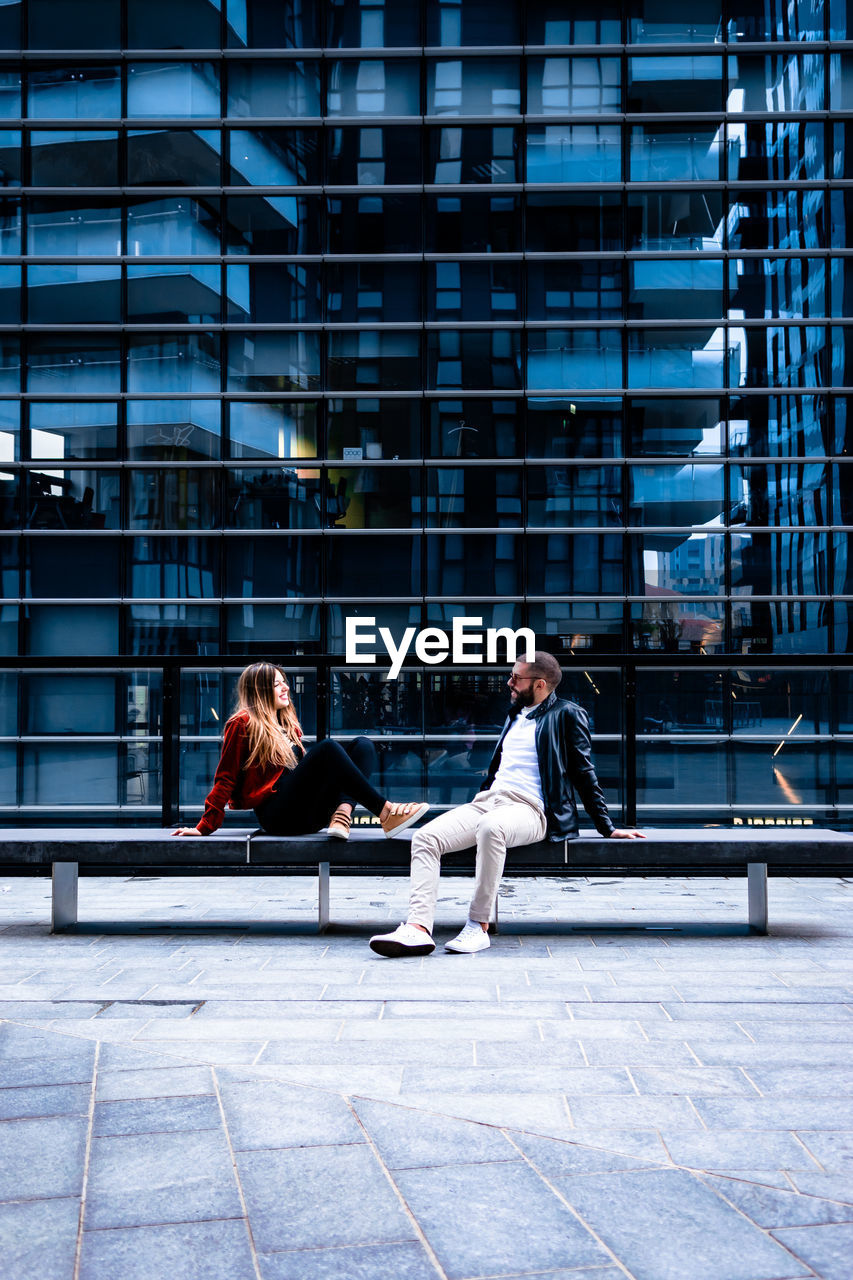 Man and woman sitting on seat against building in city