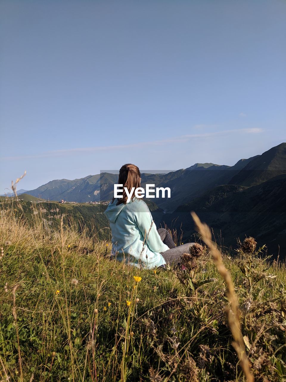 Woman sitting on grass against mountains and sky