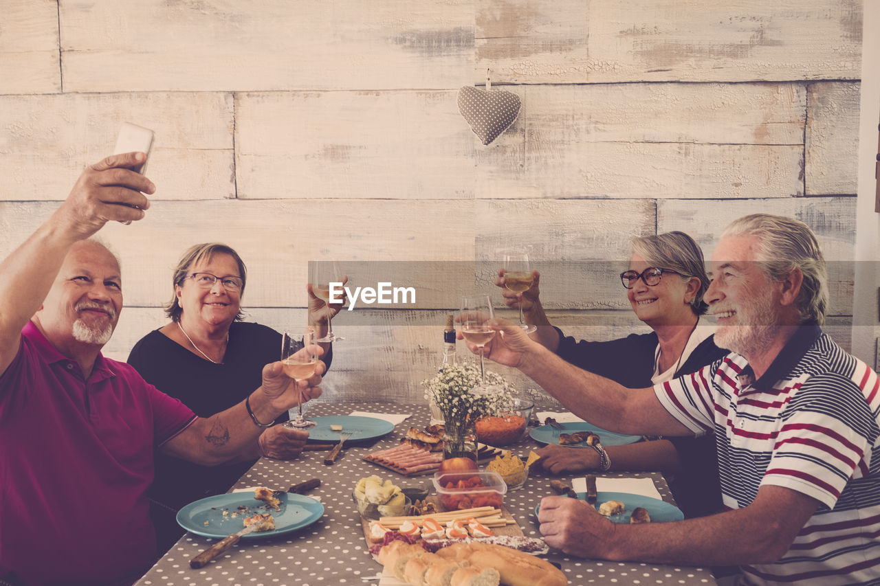 Happy friends toasting drinks while taking selfie at table