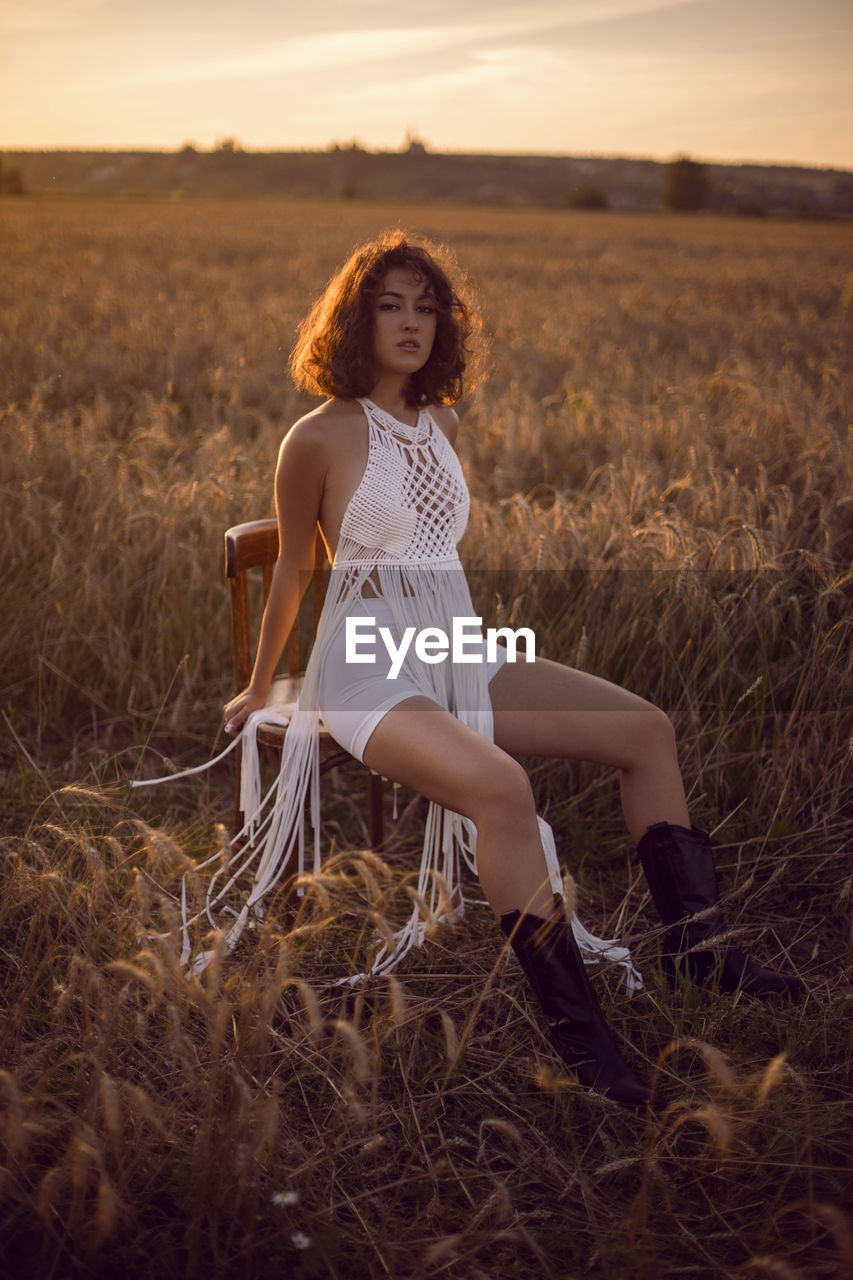  portrait of a curly-haired woman in white clothes dress sit on a field with dry grass in autumn