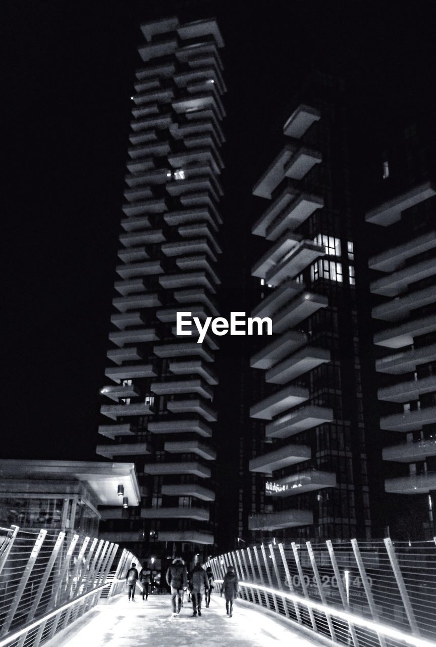 Footbridge leading towards buildings at night