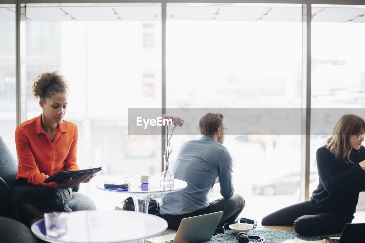 Multi-ethnic business colleagues sitting against window in cafeteria at office