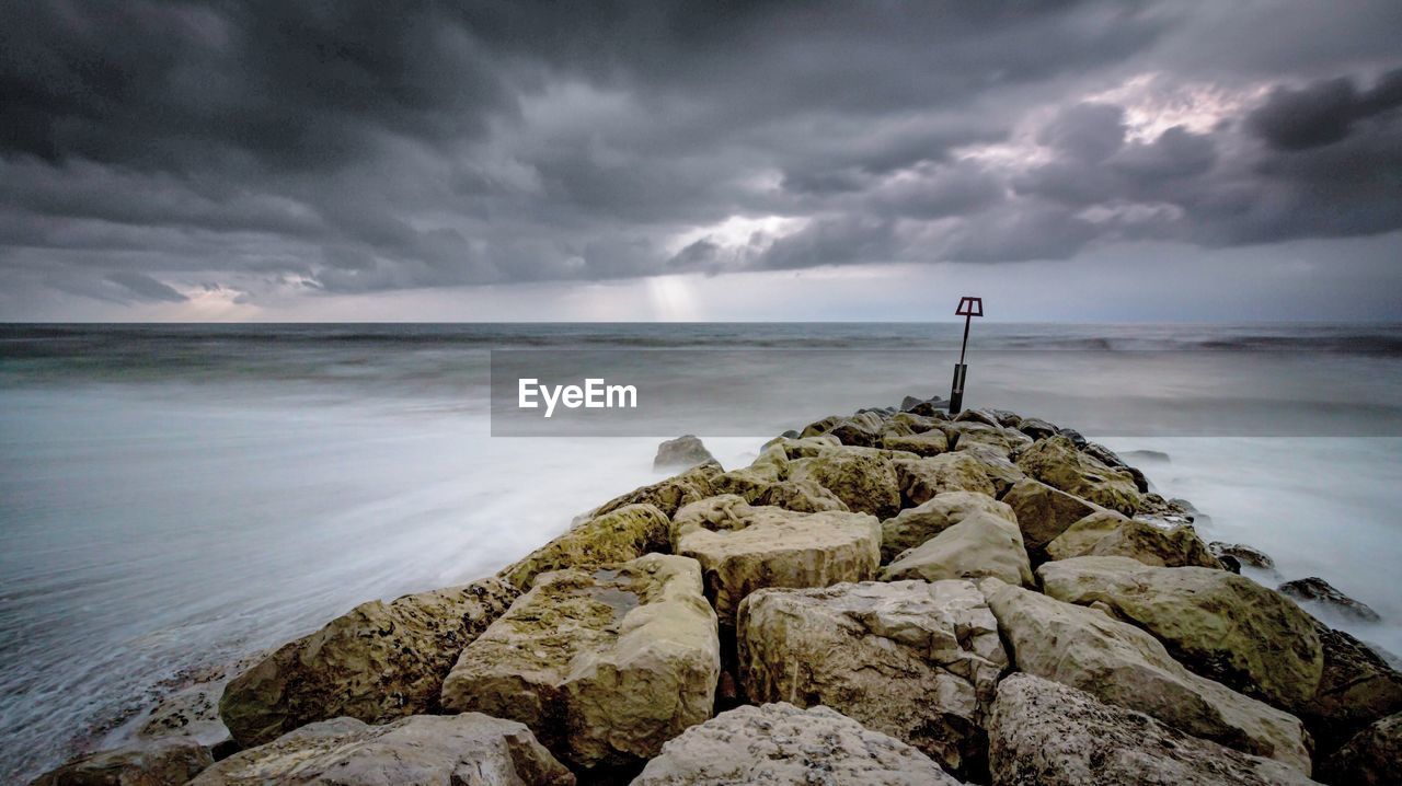 Groyne in sea against cloudy sky