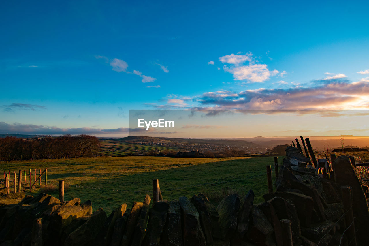 sky, landscape, horizon, environment, sunset, evening, dusk, nature, land, cloud, scenics - nature, field, rural scene, agriculture, beauty in nature, plant, sunlight, blue, no people, mountain, farm, tranquility, sun, outdoors, crop, tranquil scene, grass, travel, travel destinations, architecture, non-urban scene, twilight, horizon over land, food and drink, rural area, wood
