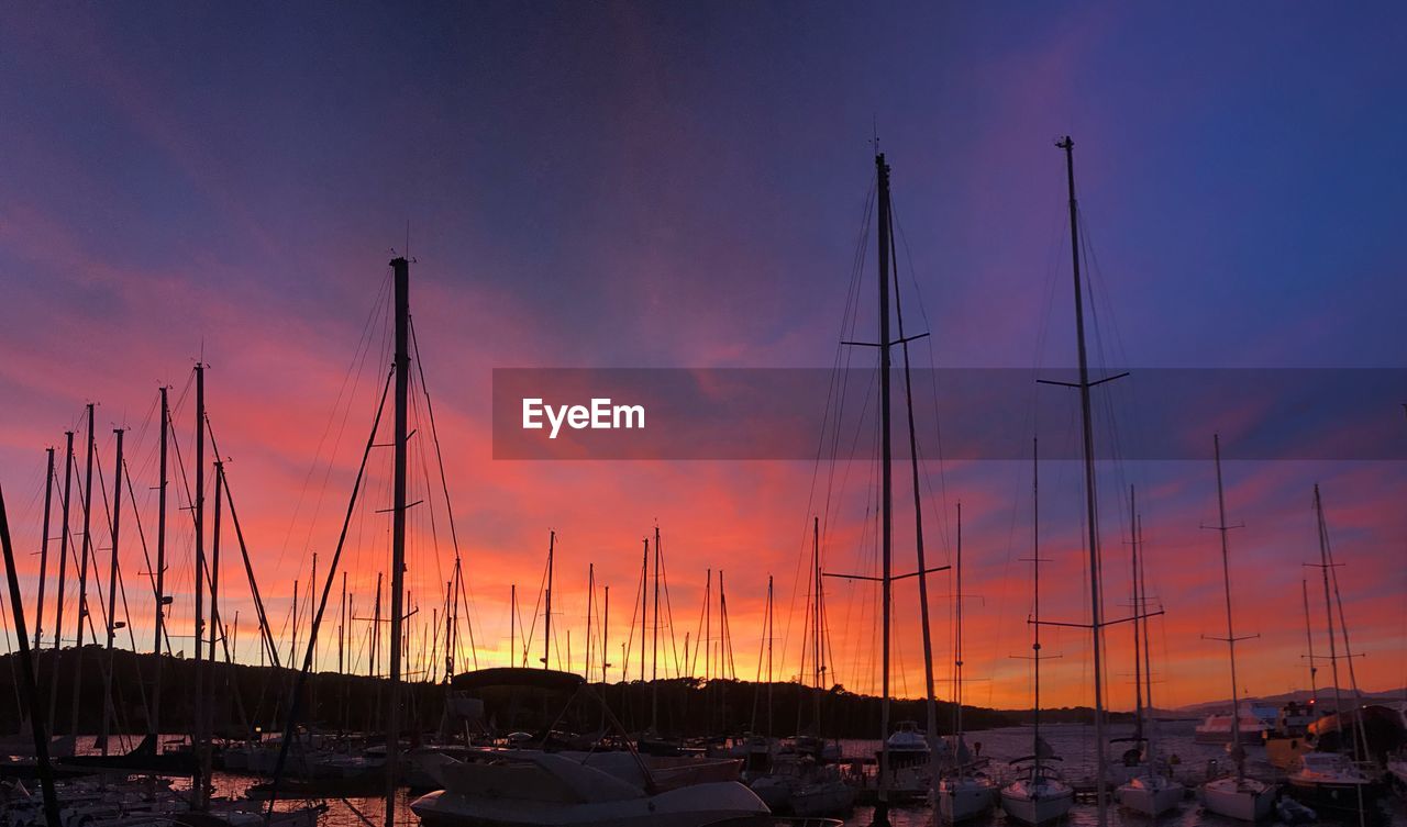 Sailboats moored at harbor against sky during sunset