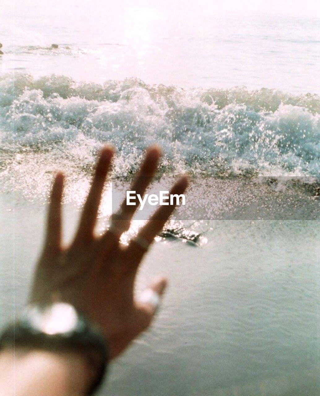 Cropped image of hand on glass window against waves in sea