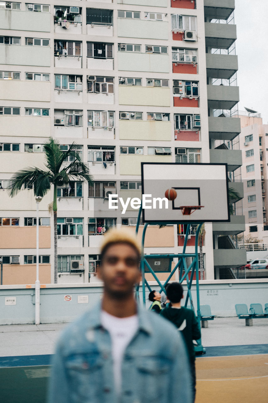 PORTRAIT OF MAN STANDING IN CITY AGAINST BUILDINGS