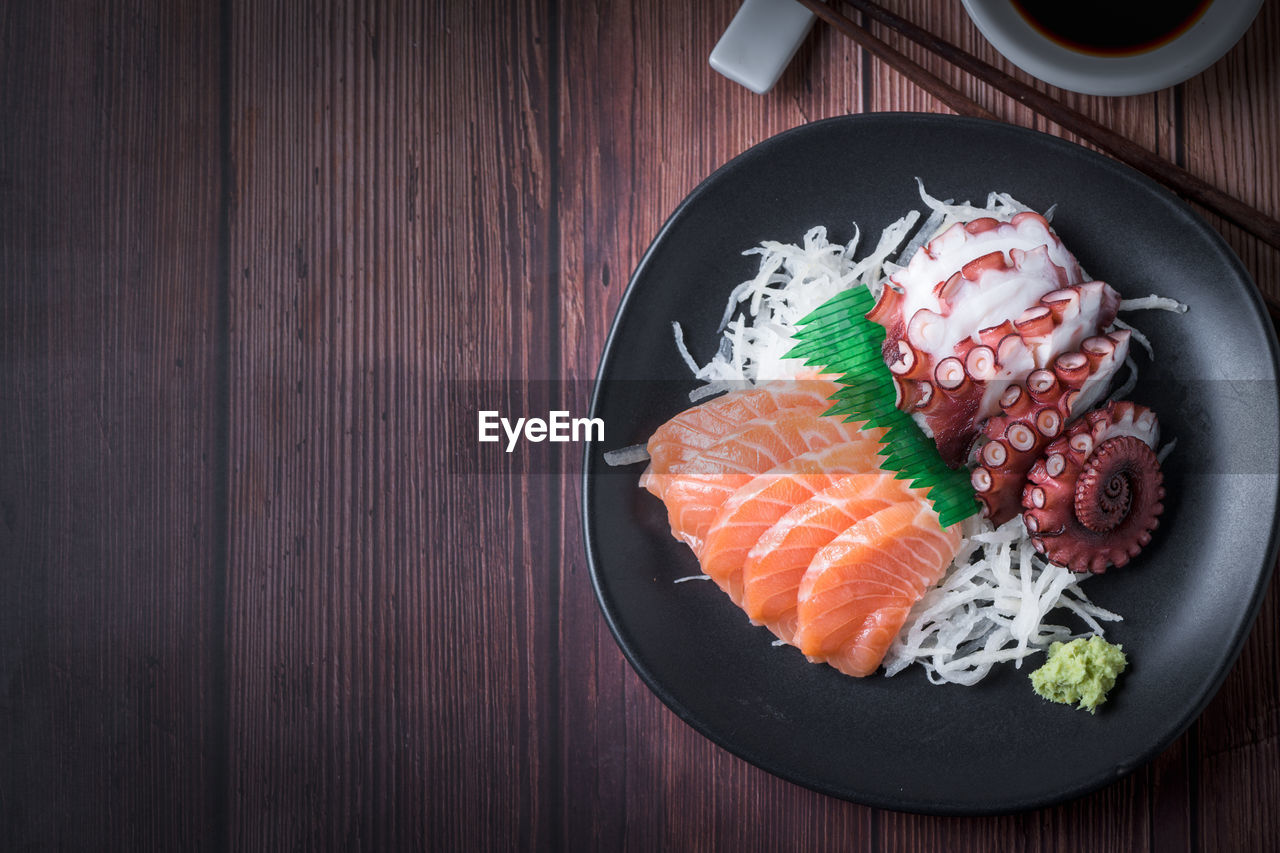 Salmon and tako sashimi on black dish with chopsticks, japanese food, wood background and copy space