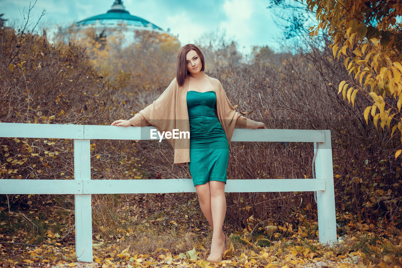 PORTRAIT OF SMILING YOUNG WOMAN STANDING BY TREE