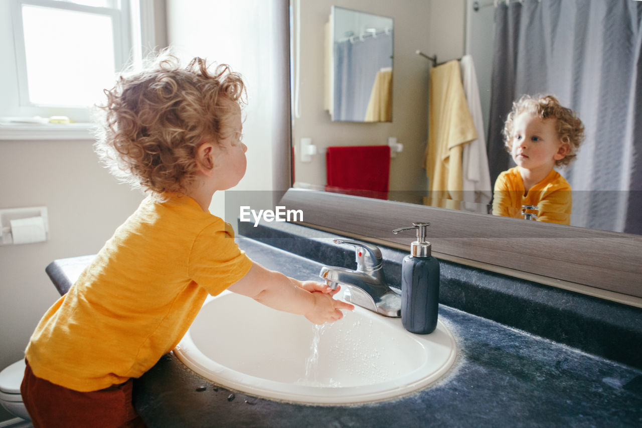 Little caucasian boy toddler washing hands in bathroom at home. health hygiene and morning routine 