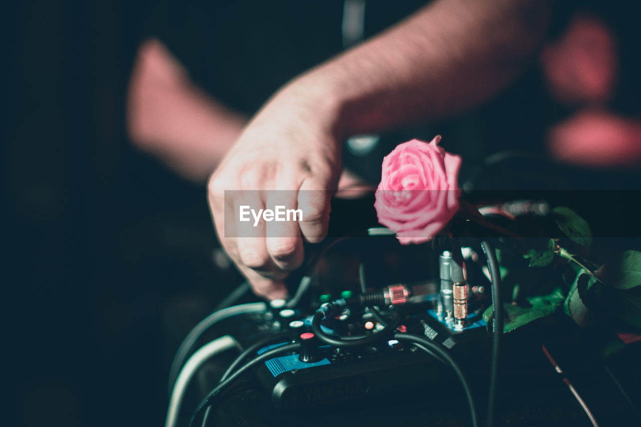 Cropped hands of man with pink rose on sound recording equipment in nightclub