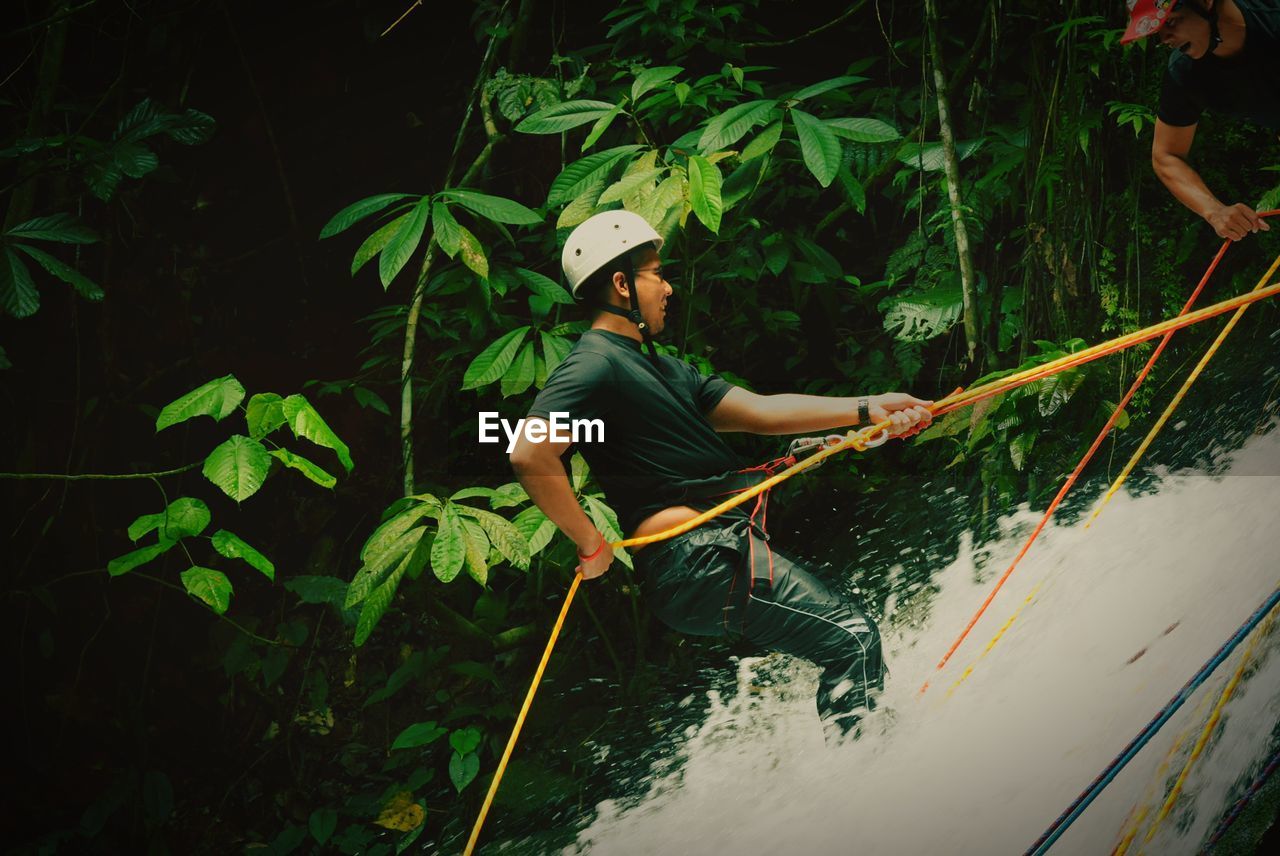 Side view of man rappelling on waterfall