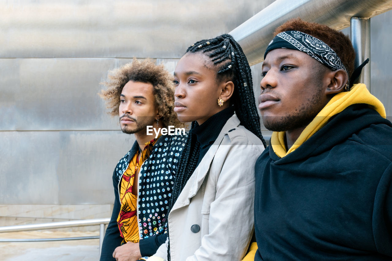 Serious unemotional young african american friends in casual informal clothes standing on stairway looking away while spending time together in city