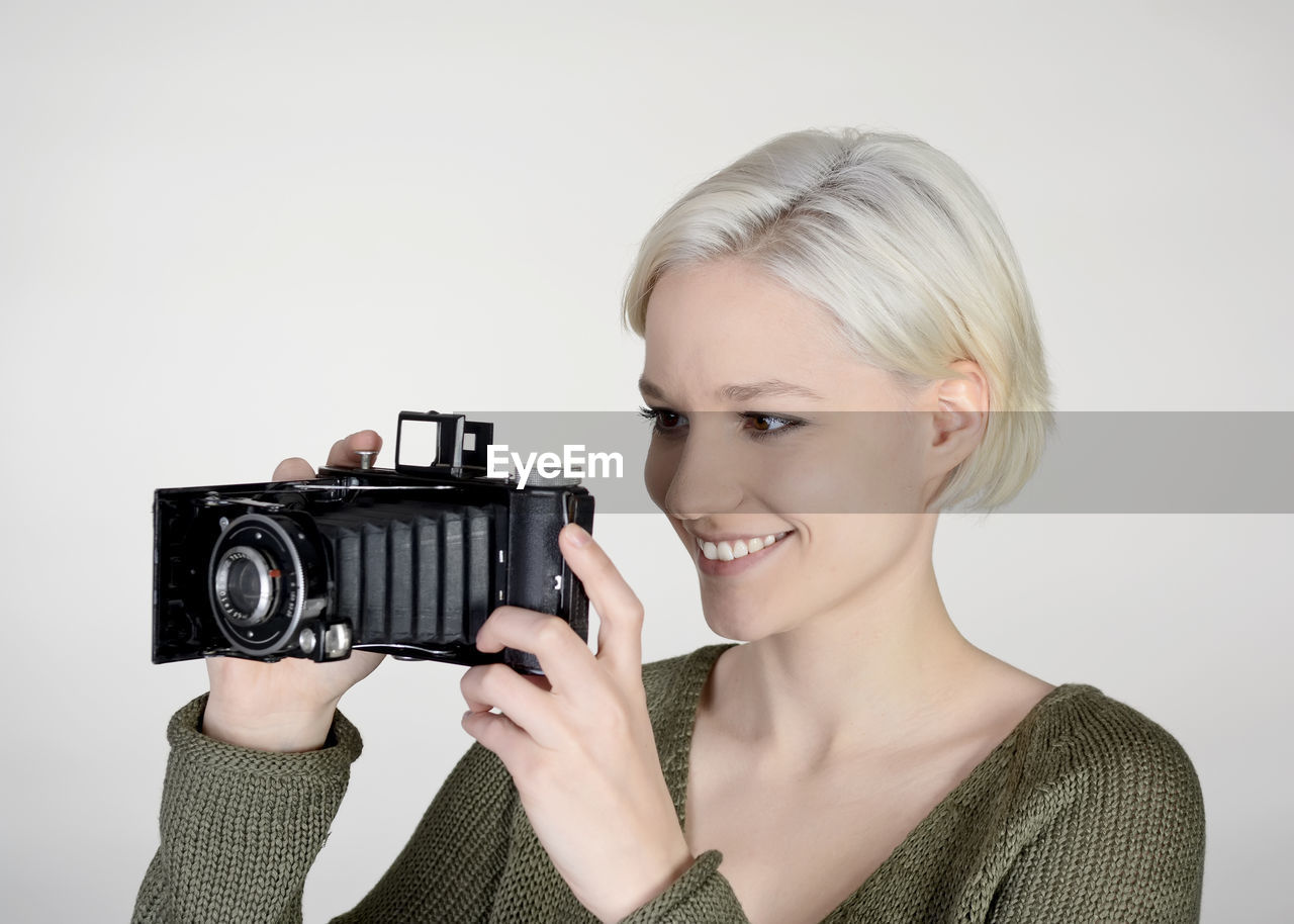 Close-up of young woman photographing while standing against white background