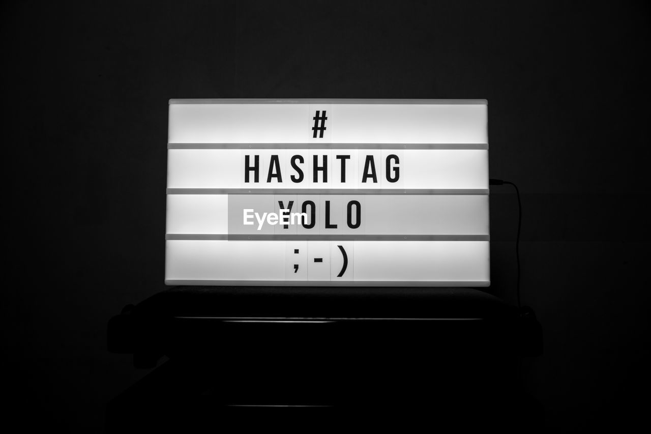 Close-up of placard with hashtag and yolo text over black background