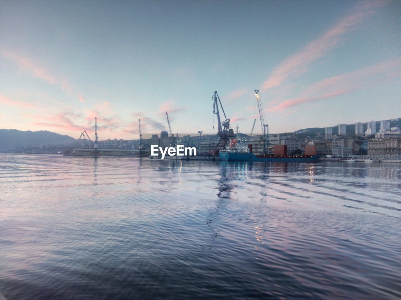 Cranes at harbor against sky during sunset