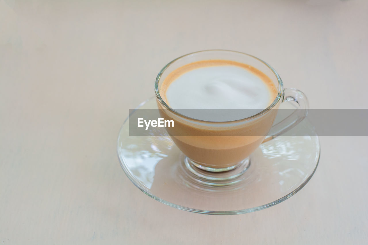 Top view of hot cappuccino coffee and milk froth in clear cup on wooden table in coffee shop.
