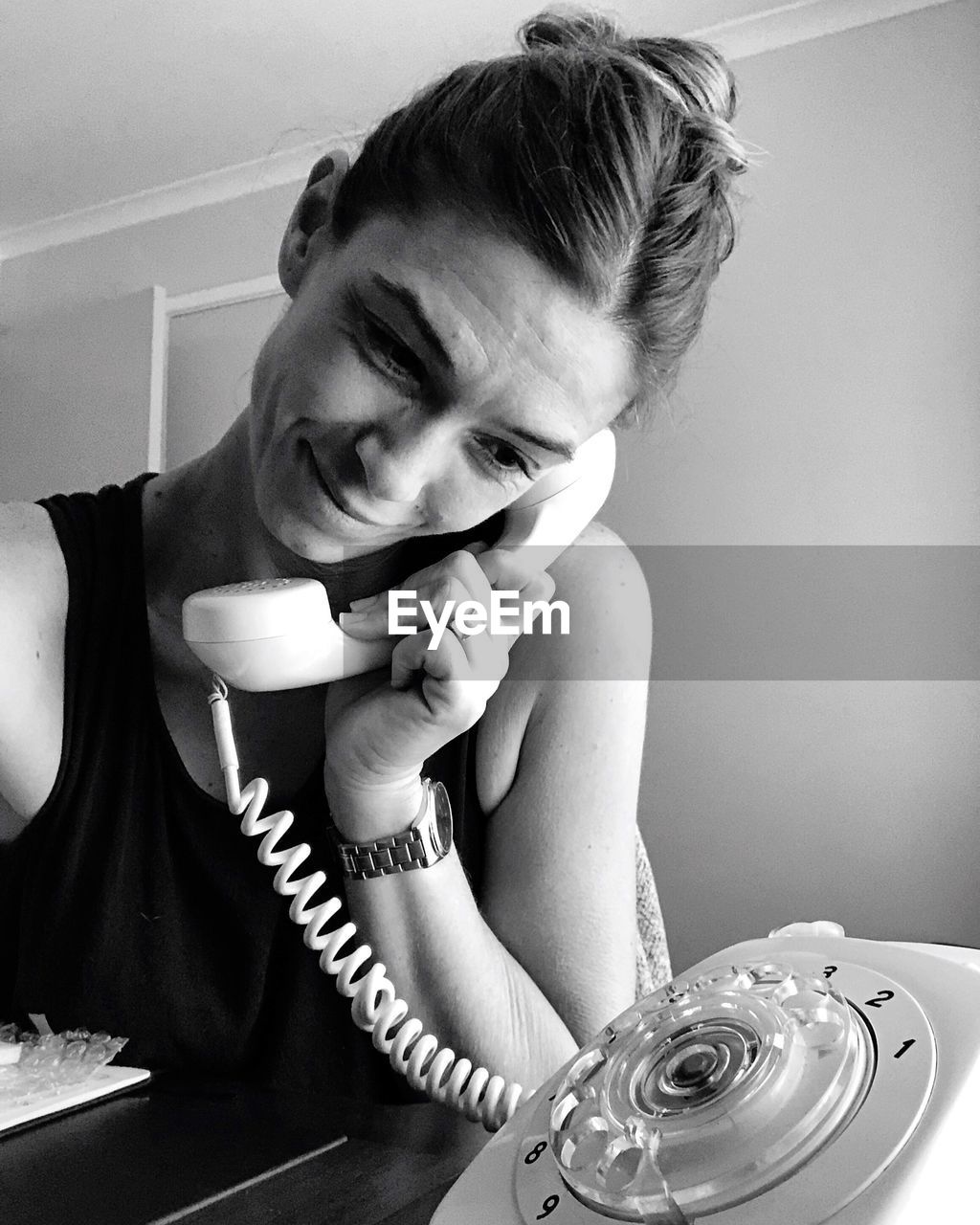 Smiling woman talking on old-fashioned rotary phone at home