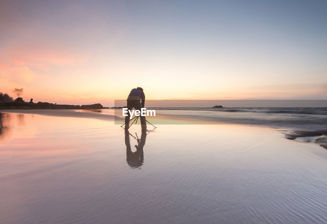 FULL LENGTH OF SILHOUETTE PERSON ON SHORE AGAINST SKY DURING SUNSET