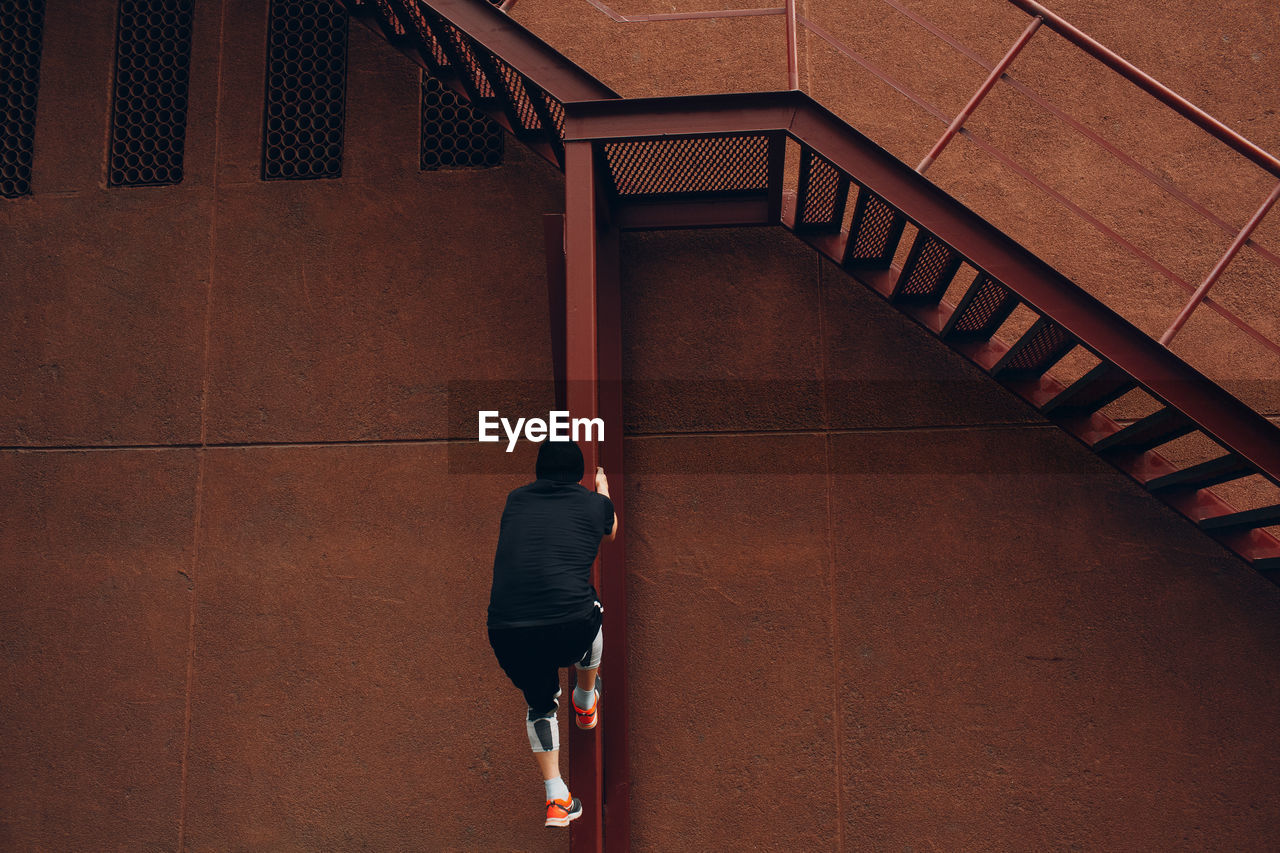 Man climbing on metal column against brown wall