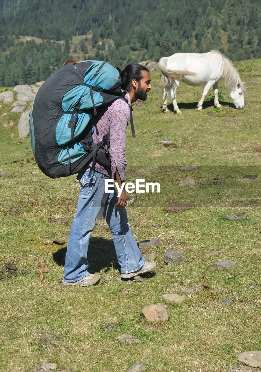 Side view of a male tourist walking on the mountain with carrying parachute backpack