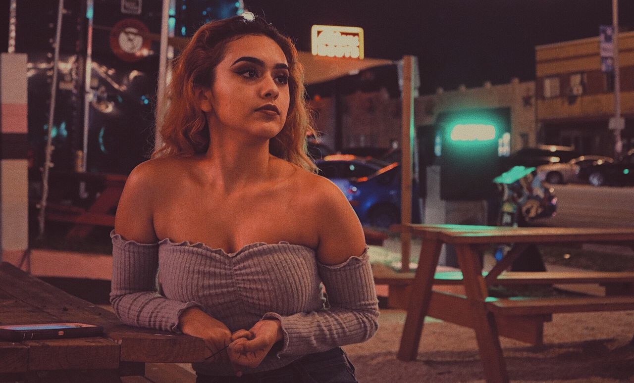 Young woman in off shoulder dress standing outdoors at night