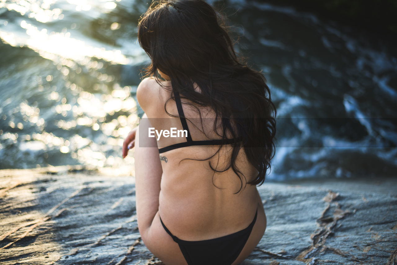 Young latina woman sitting by the ocean at golden hour in summertime