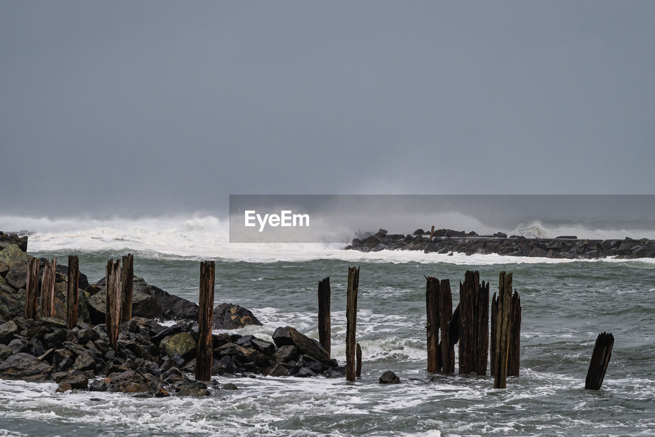 water, sea, ocean, shore, wave, coast, land, sky, beach, scenics - nature, nature, environment, winter, beauty in nature, snow, wind wave, body of water, wood, landscape, motion, cold temperature, no people, wooden post, storm, outdoors, post, breakwater, horizon, cloud, day, tranquility, non-urban scene, rock, coastline, seascape, travel destinations, travel, tranquil scene, architecture, wind, fog, bay