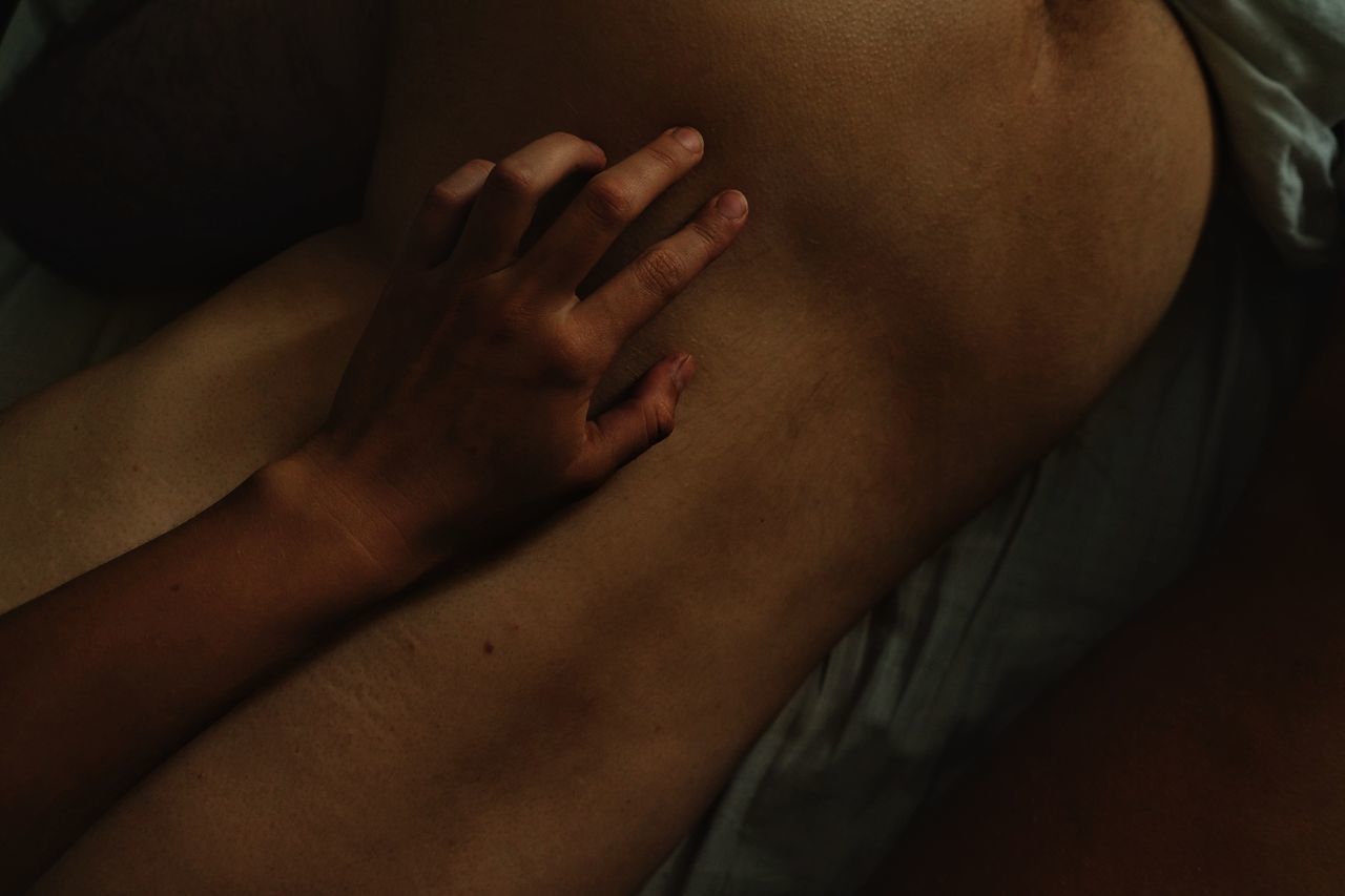 Cropped hand of woman touching shirtless man back lying on bed at home