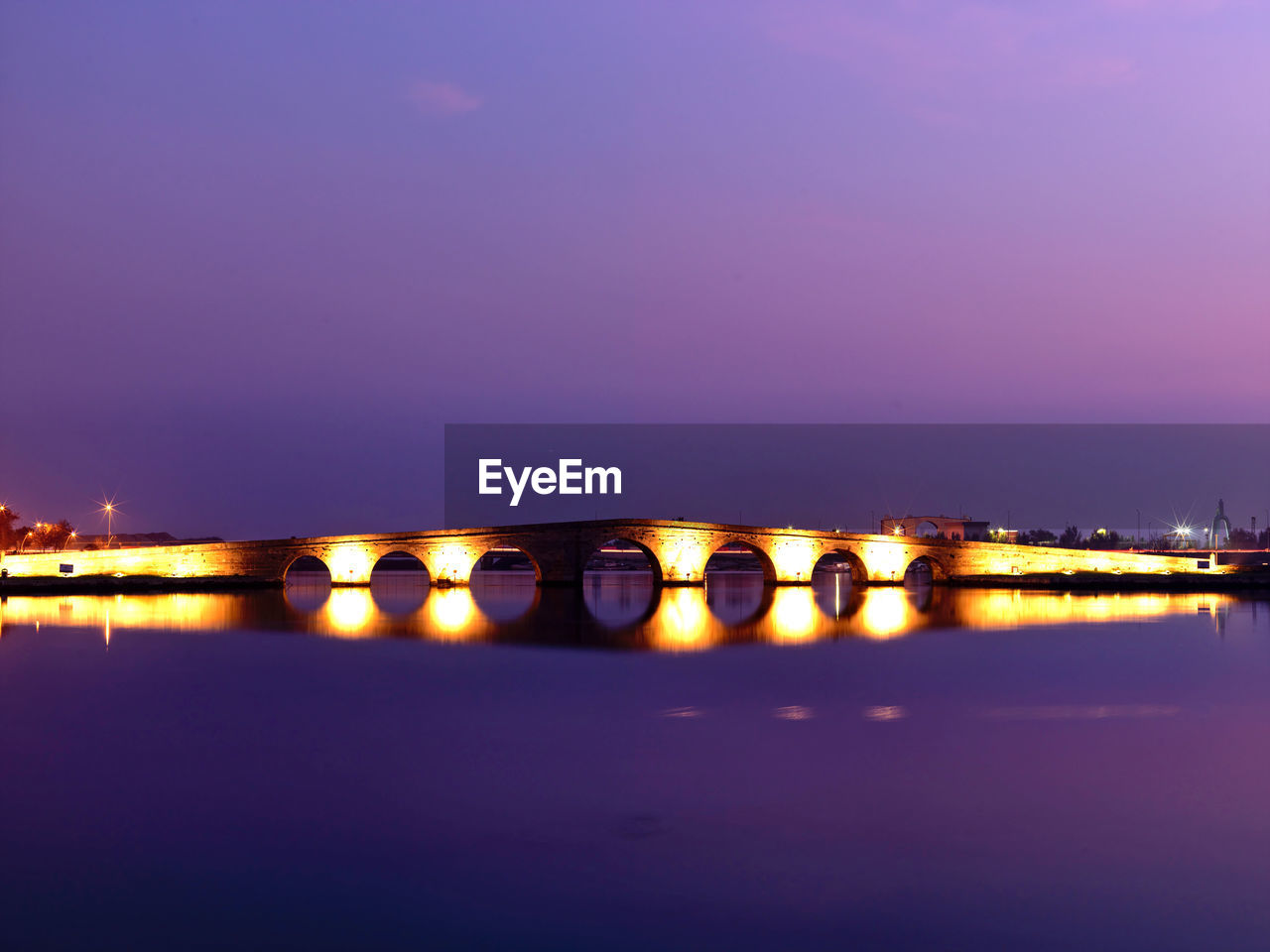 Illuminated city by sea against sky at night