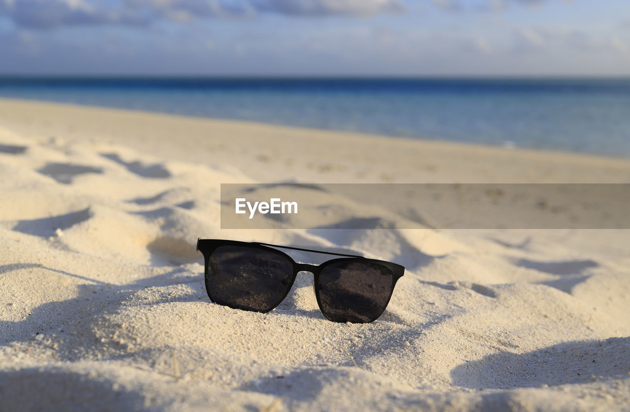 CLOSE-UP OF SUNGLASSES ON SAND