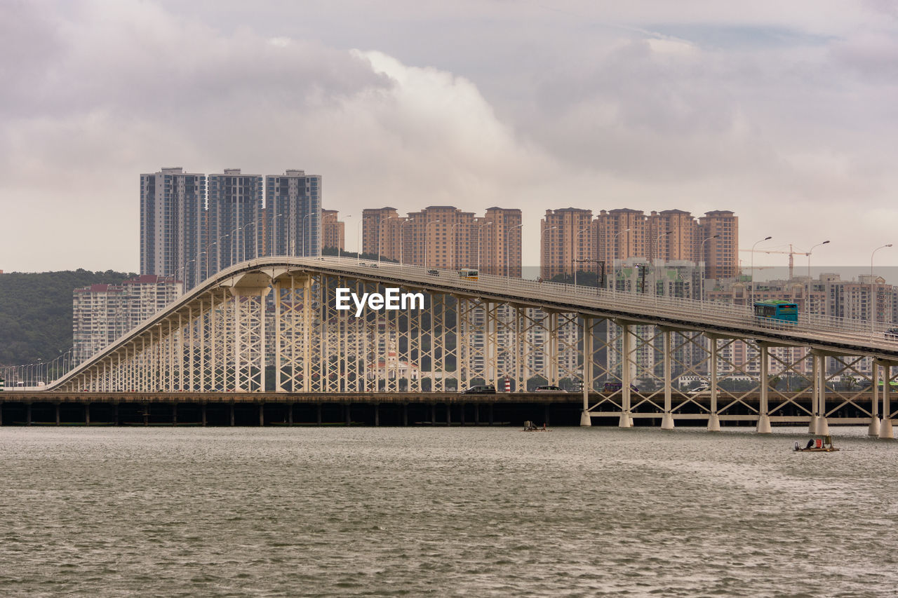 BRIDGE OVER RIVER BY BUILDINGS AGAINST SKY