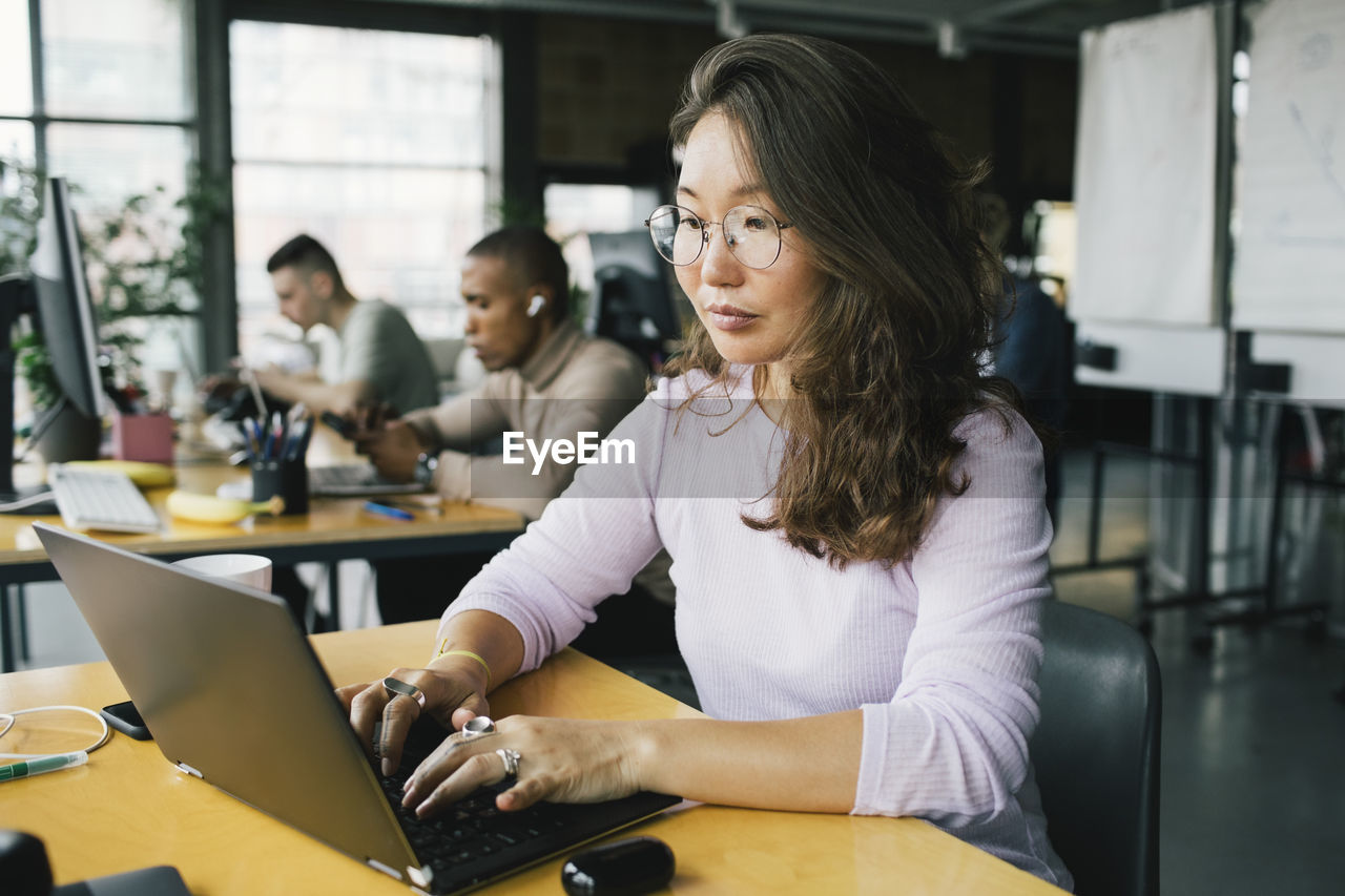 Female computer programmer coding on laptop at desk in startup company