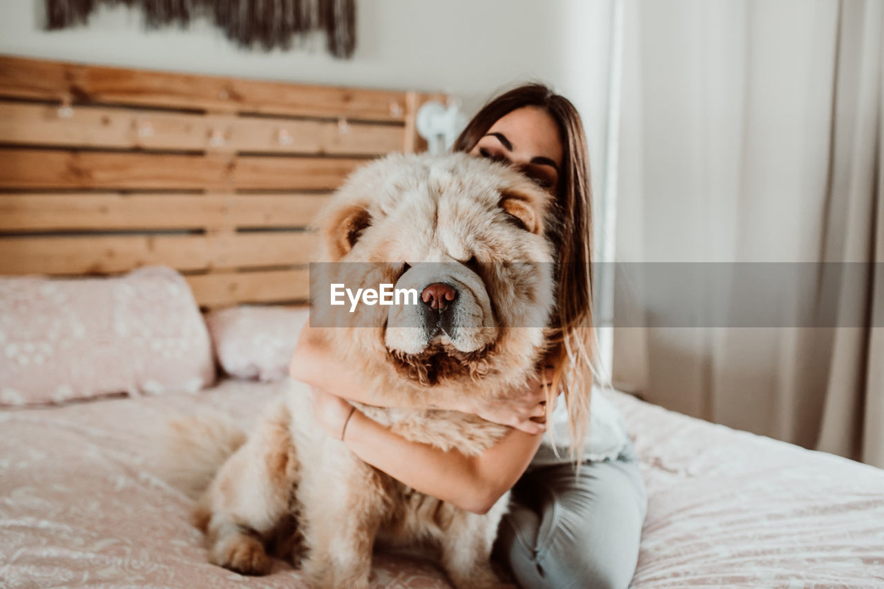 Young woman embracing dog on bed at home