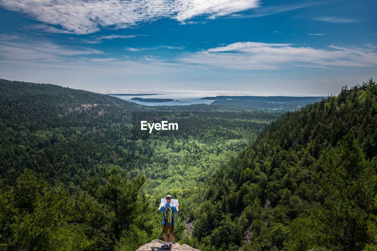 Rear view of mature man looking at landscape while standing on mountain against blue sky