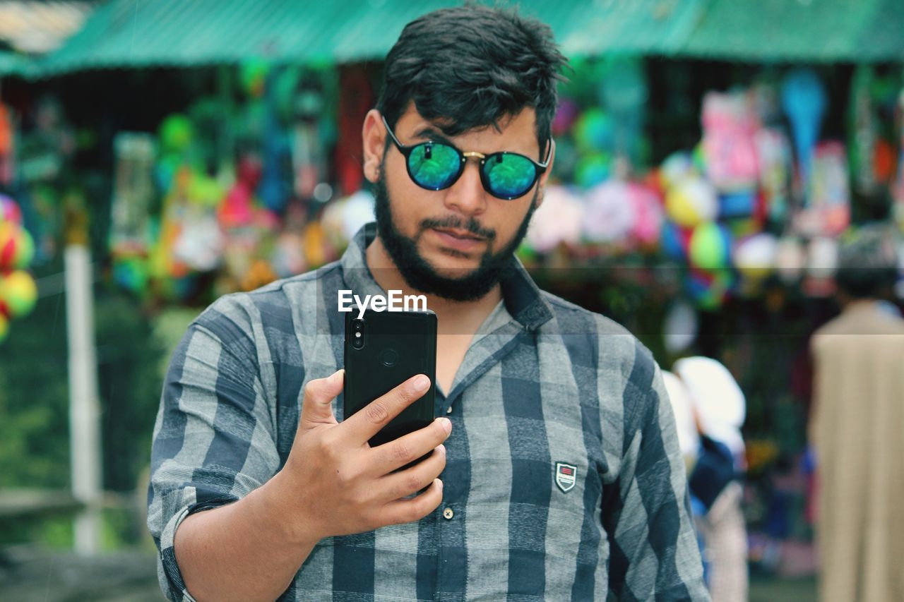 Young man wearing sunglasses using mobile phone while standing in market