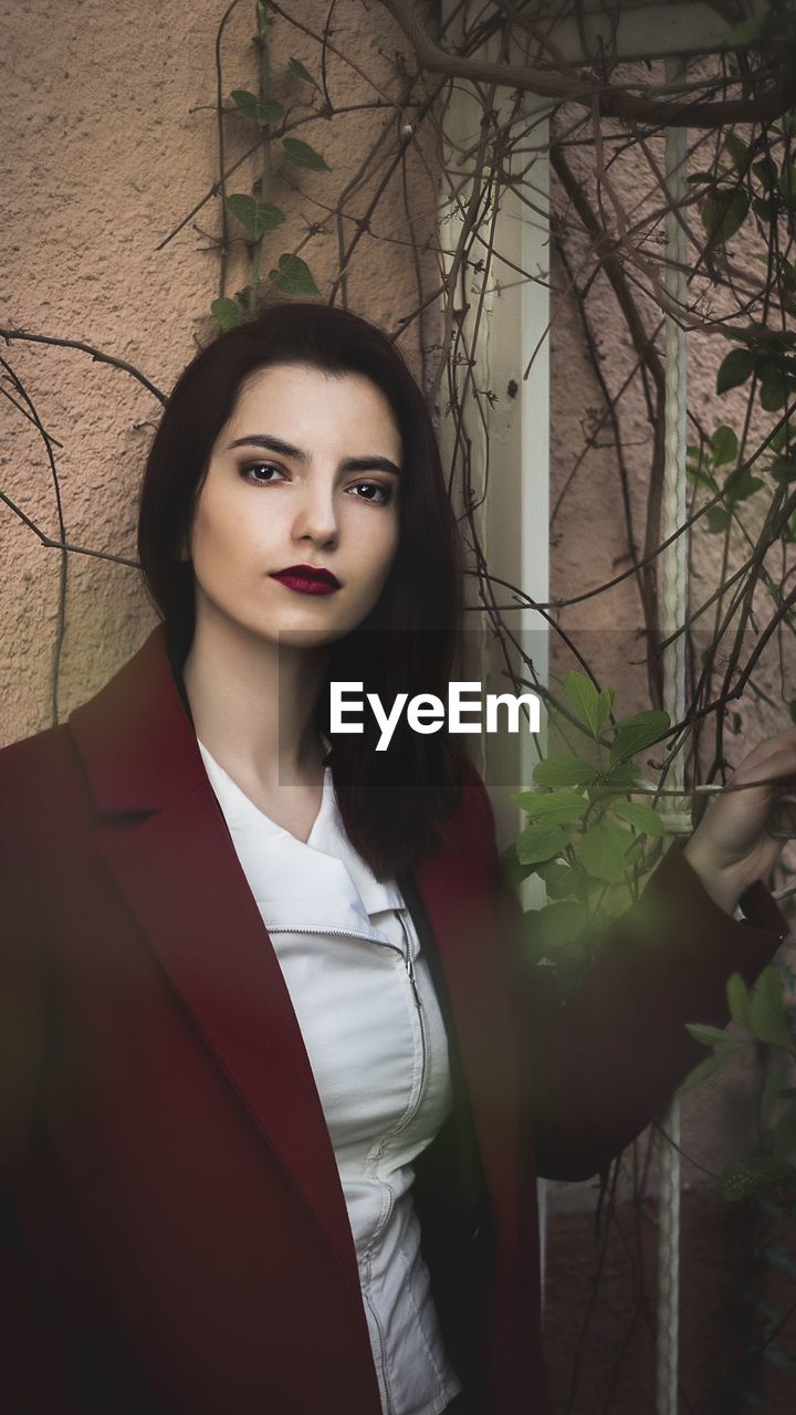 PORTRAIT OF A YOUNG WOMAN STANDING AGAINST PLANTS