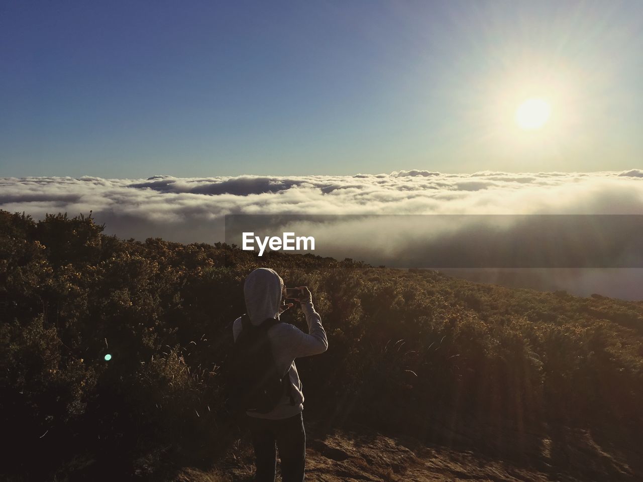 Rear view of woman photographing on mountain against sky during sunset