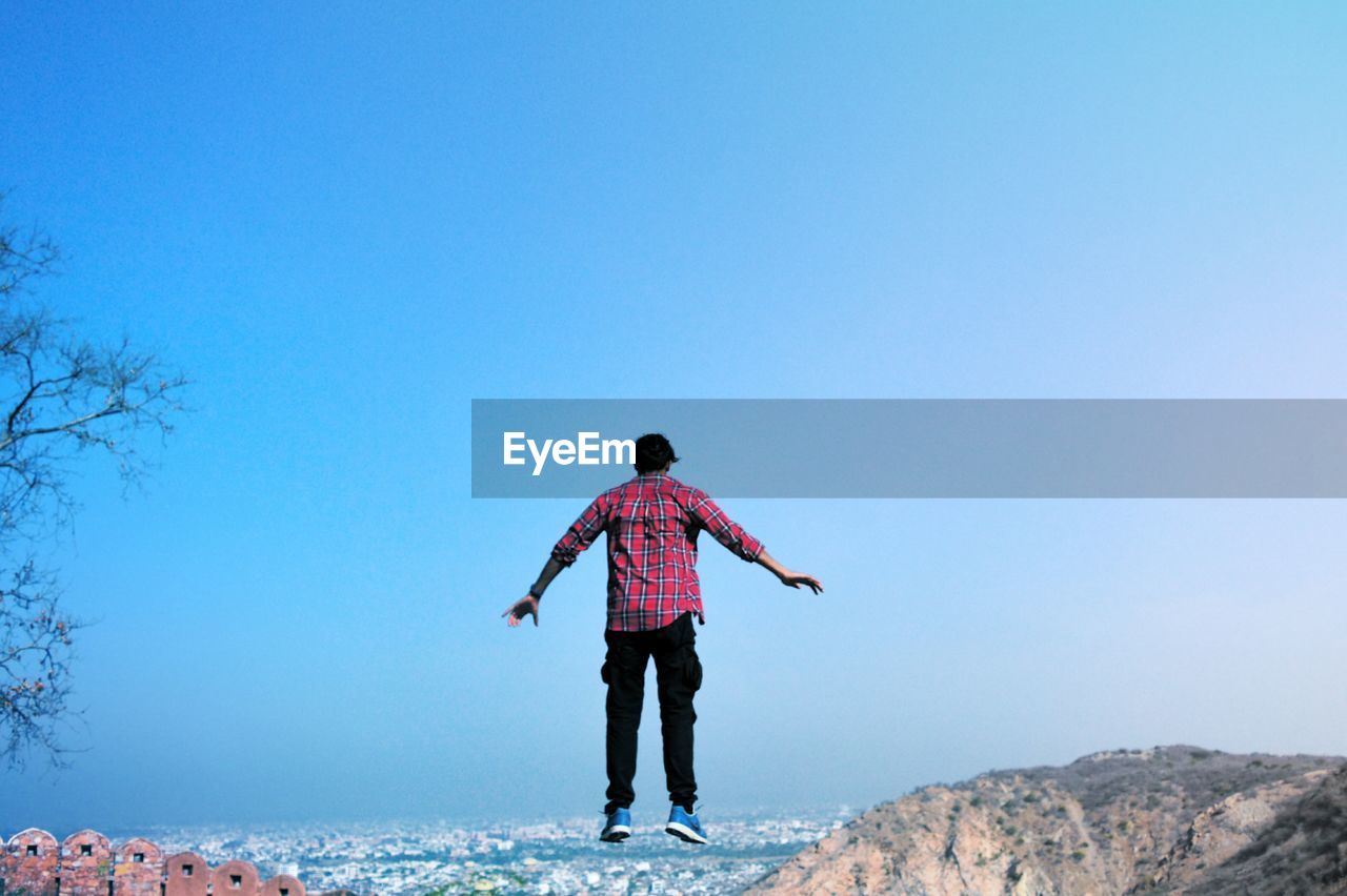 Rear view of levitating in mid-air against clear blue sky