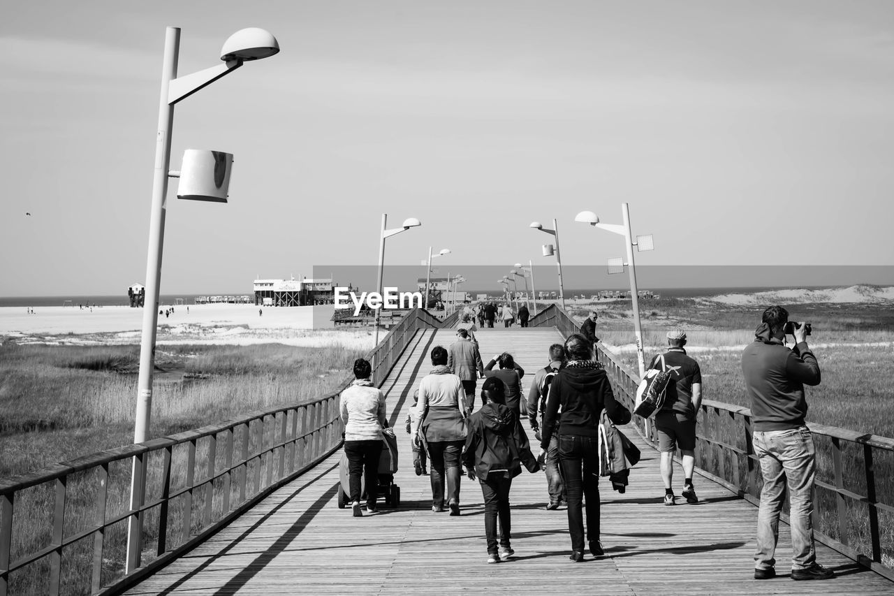 People walking on pier by sea against sky