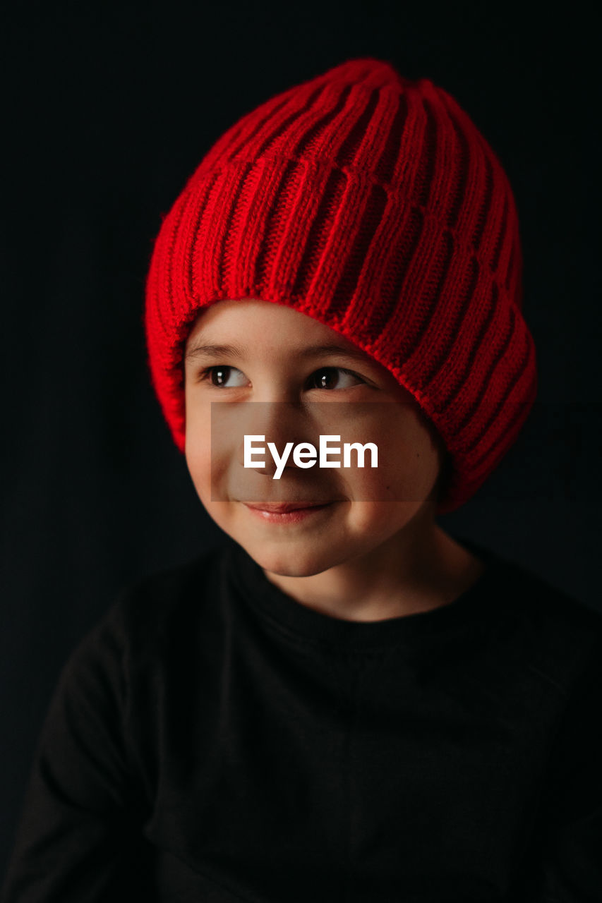 Portrait of boy in red  hat against black background
