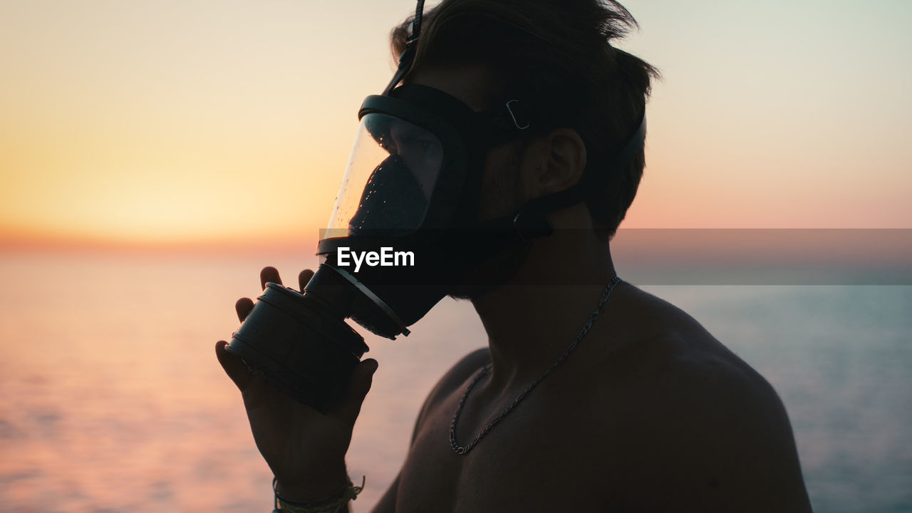 Silhouette of a boy putting on his gas mask at dawn in the ocean