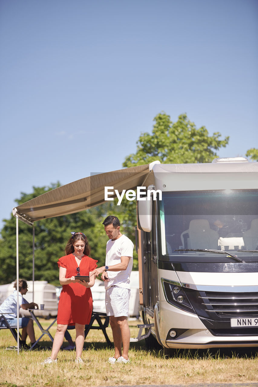 Parents discussing over digital tablet by camper van with son sitting in background