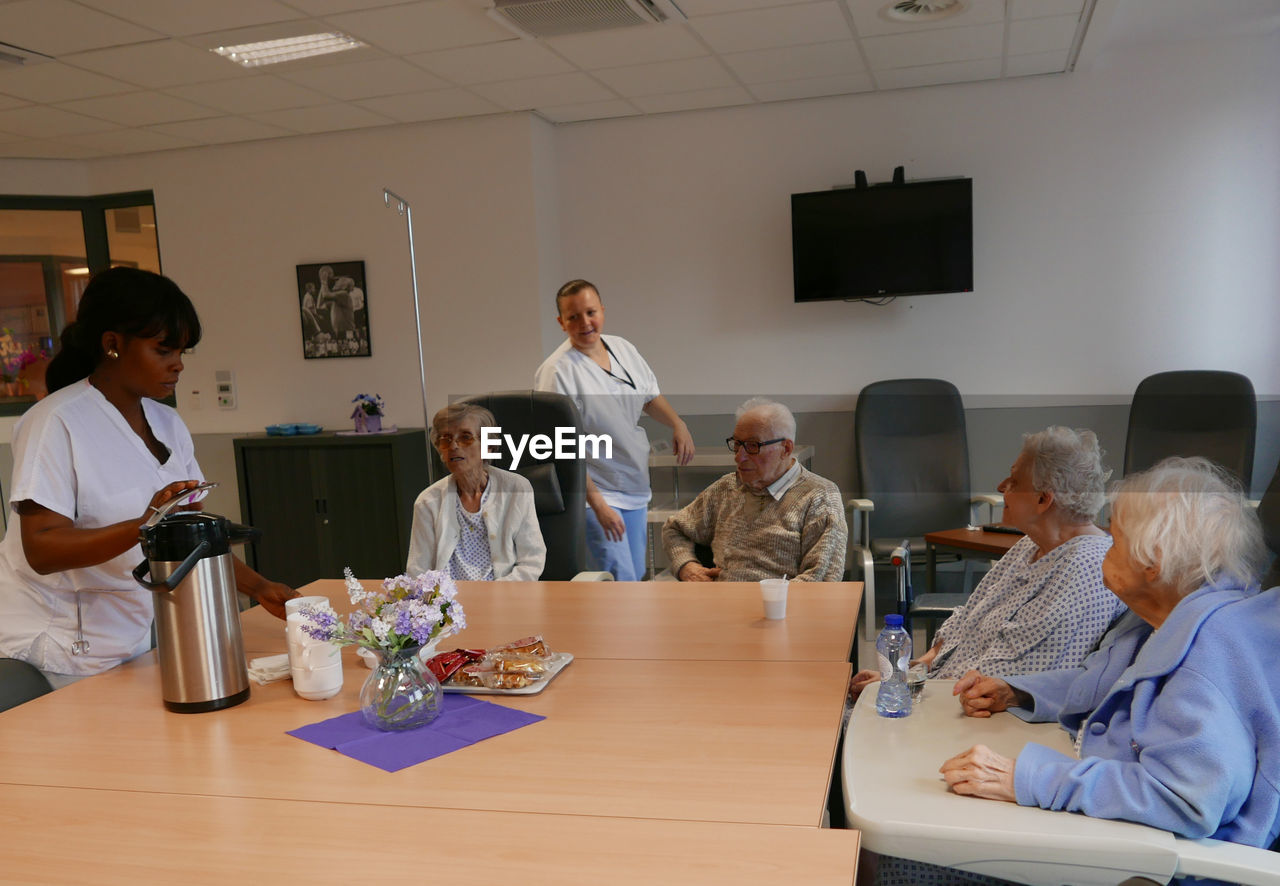 Caretakers and senior people at table in nursing home