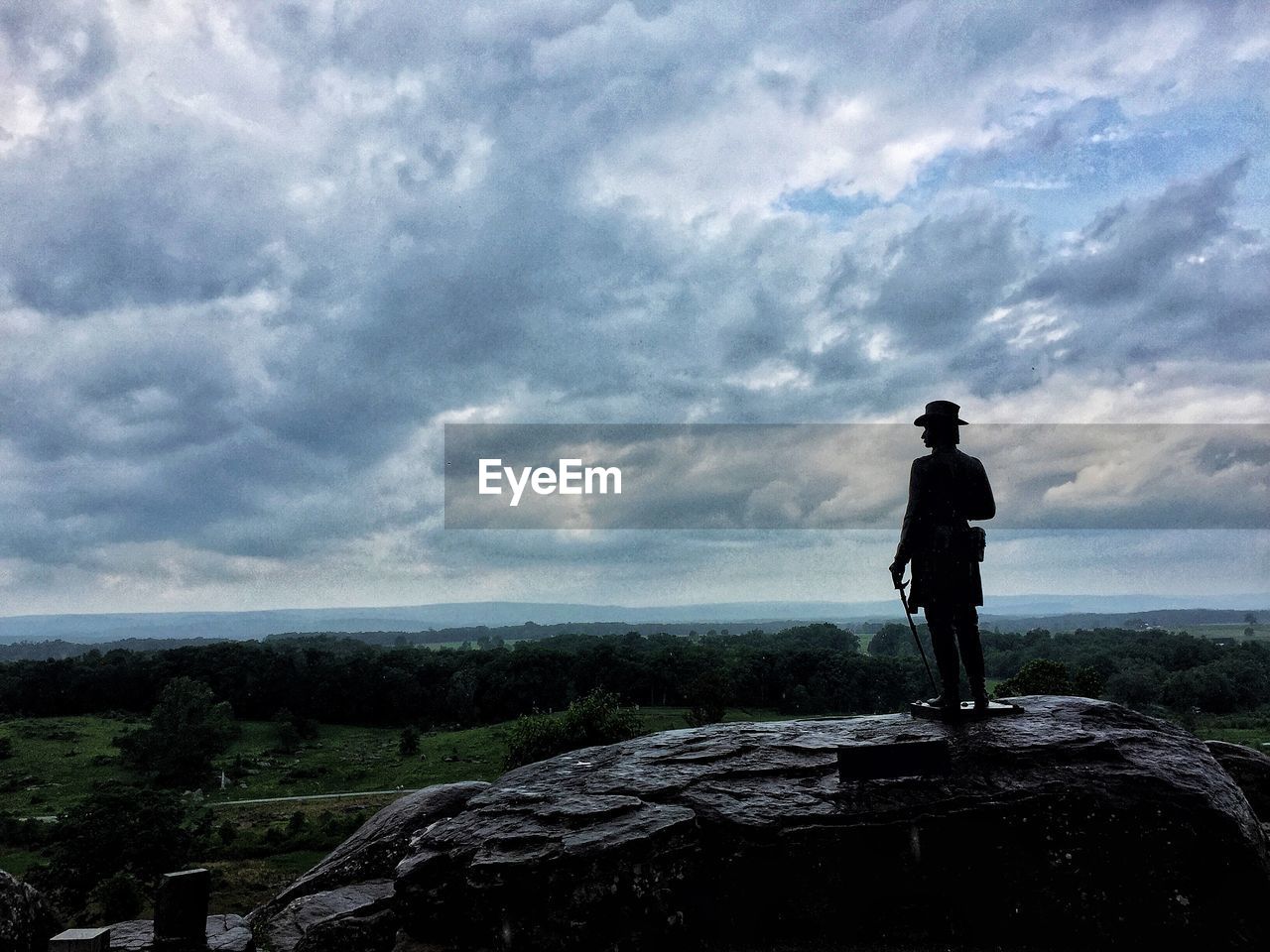 MAN STANDING ON ROCK LOOKING AT VIEW OF SKY