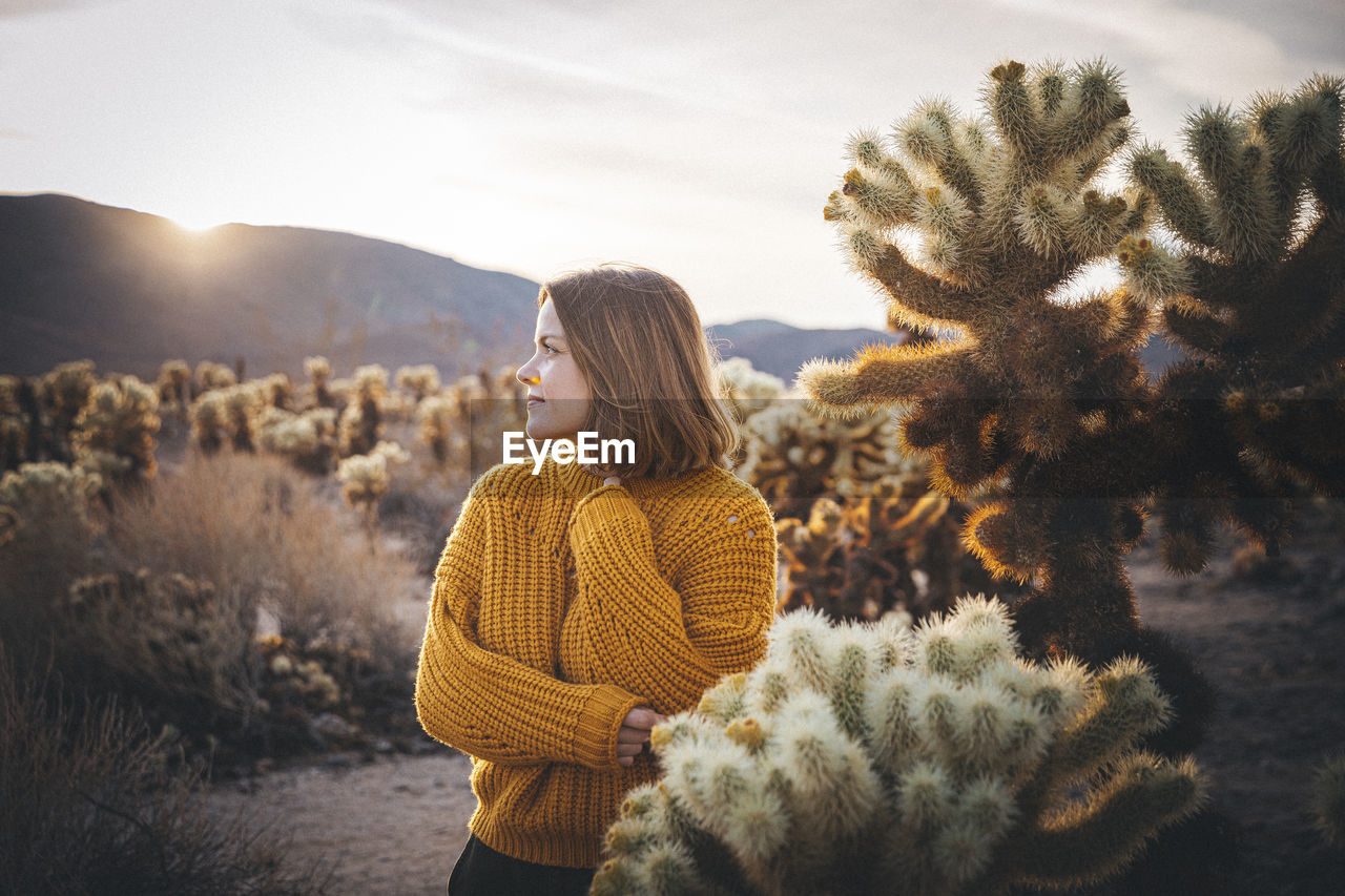 A woman is standing near a cactus in the desert of california