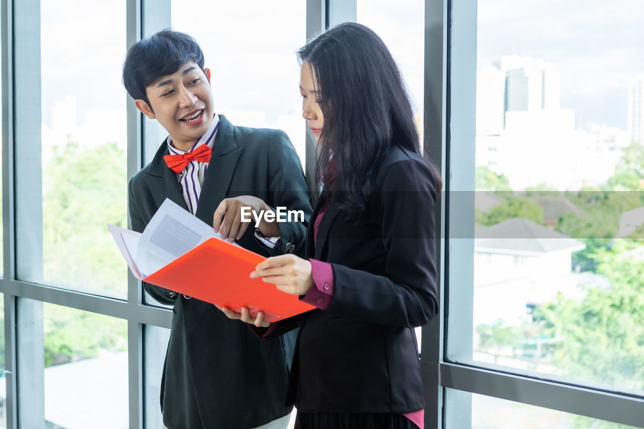 YOUNG COUPLE STANDING BY WINDOW AT OFFICE