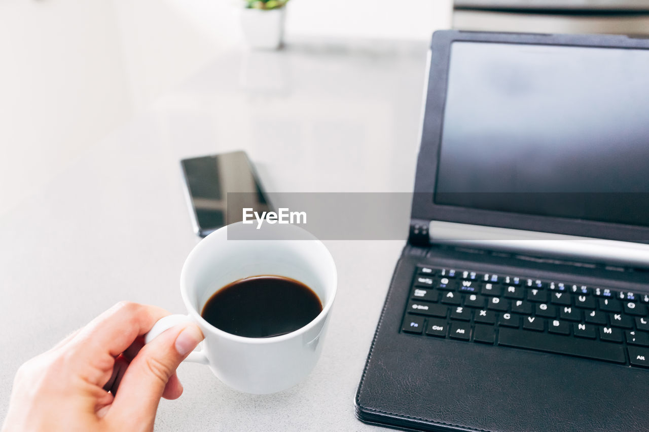 Cropped image of hand holding coffee cup on table