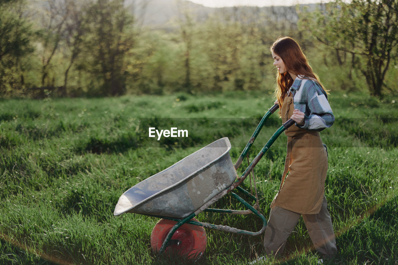 Side view of woman walking on grass with wheelbarrow